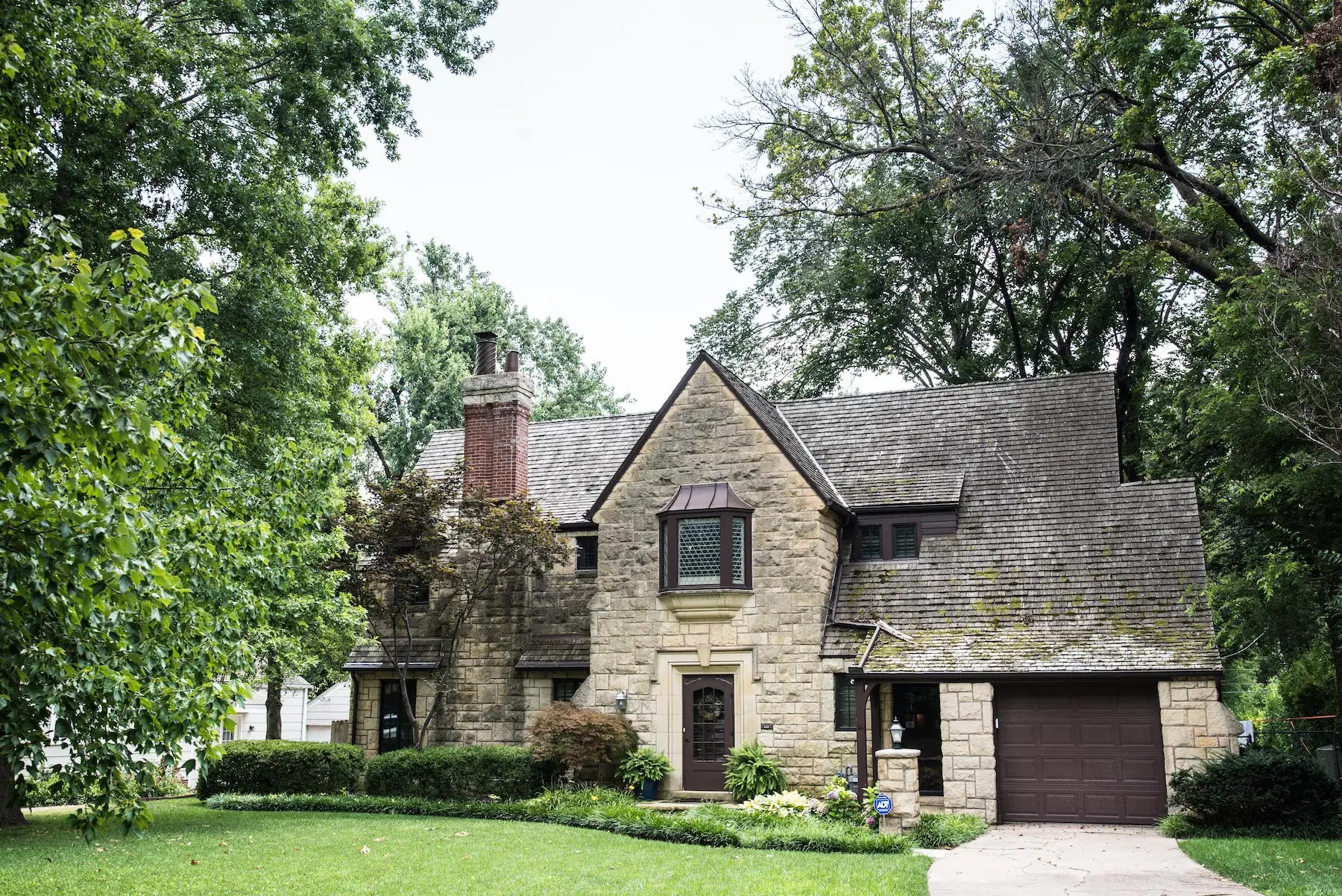 Stone two-story home with a steep gabled roof among mature trees